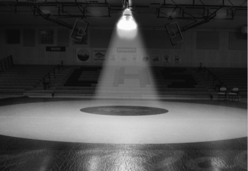 Spotlit wrestling mat in empty gymnasium